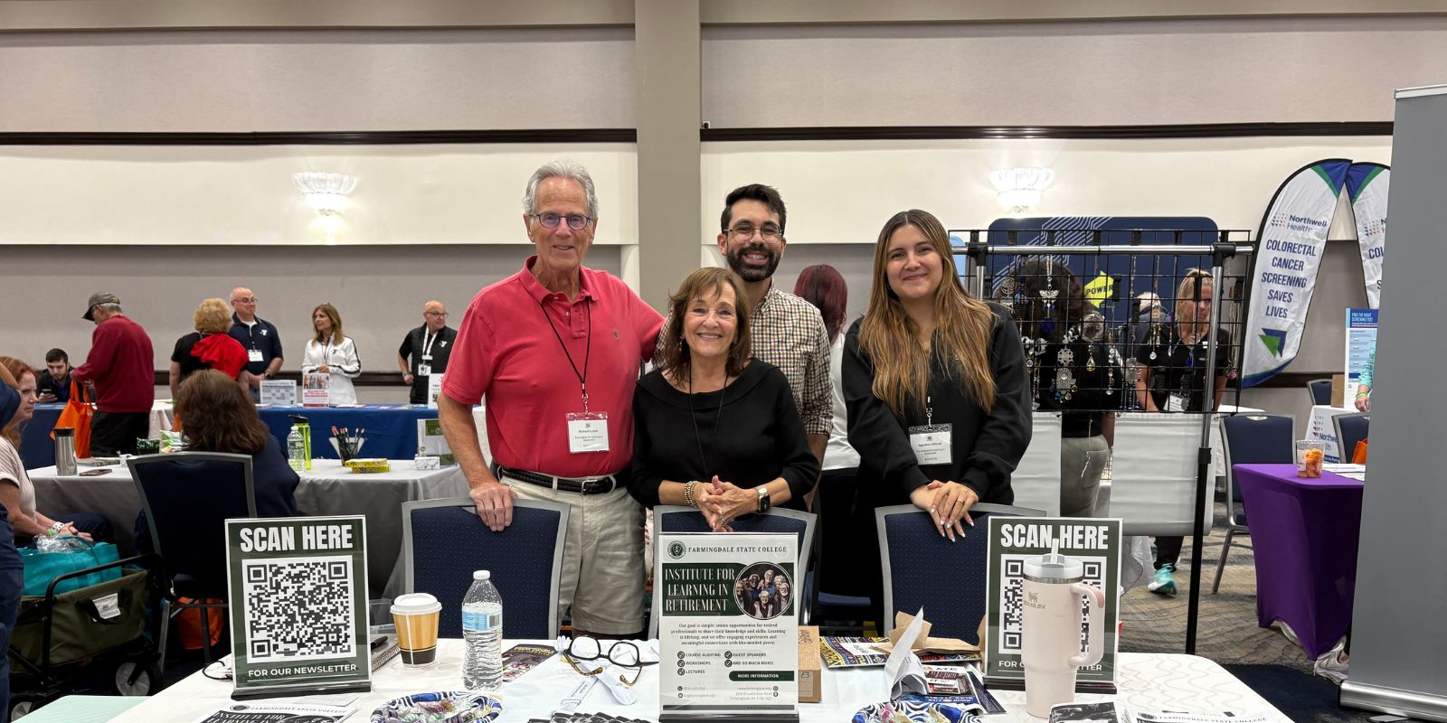 4 representatives of Farmingdale State College’s program stand behind their table. There are signs and other items on their table