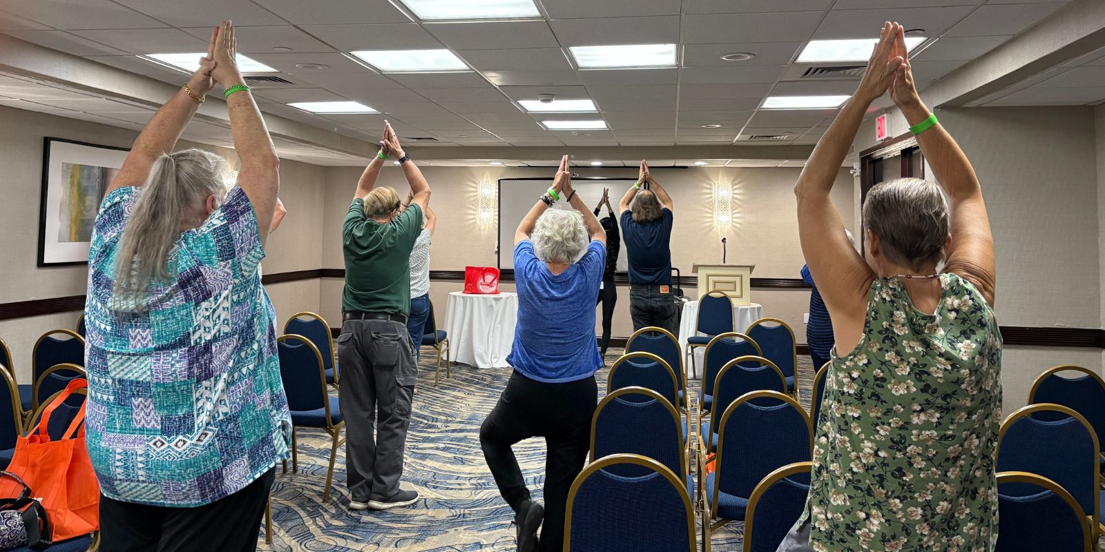Yoga class with everyone having their arms clasped above their heads