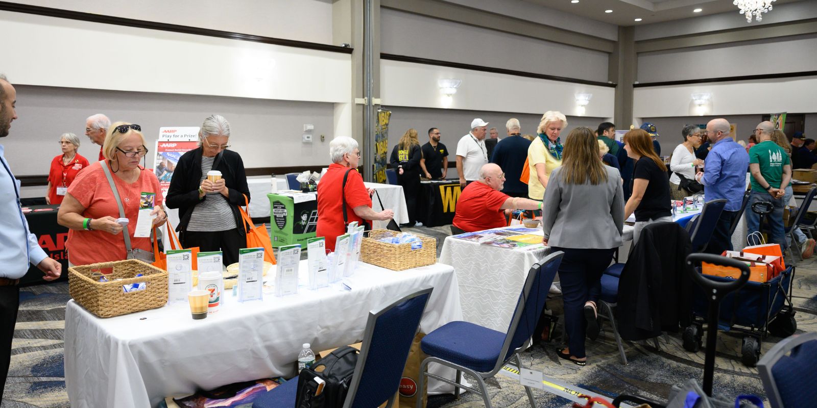 Many attendees can be seen looking at the exhibitor tables which are lined up in a row.
